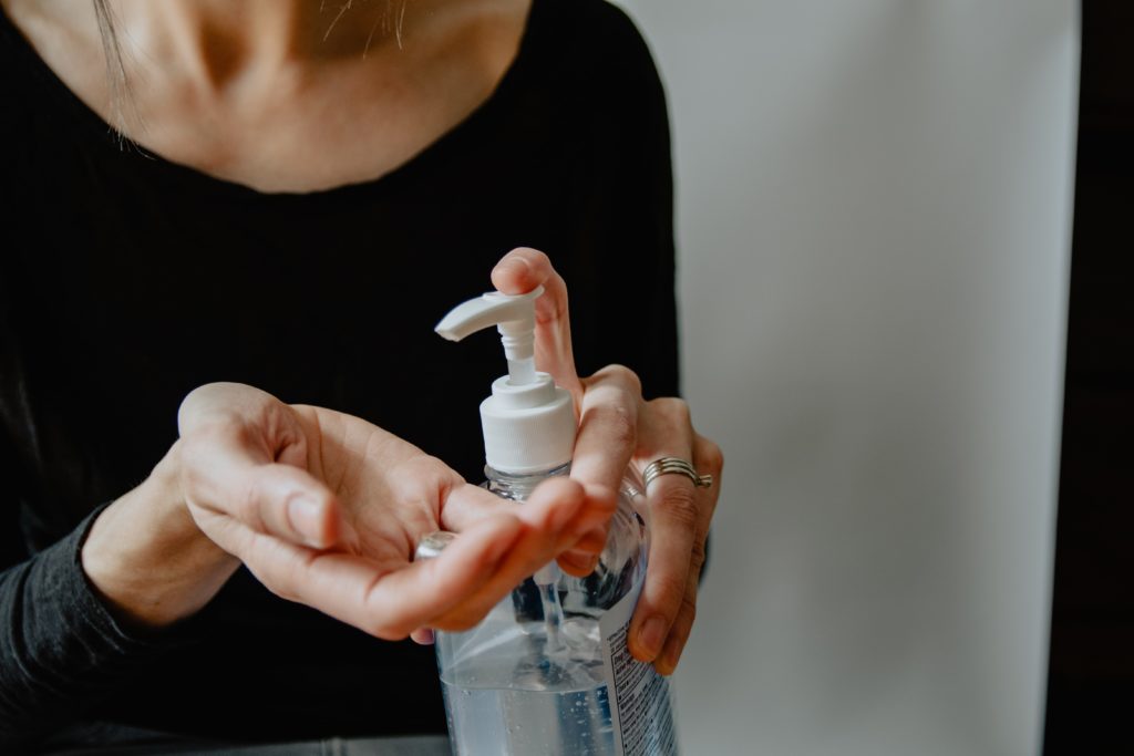 Person pressing a pump bottle to apply hand sanitizer onto their palm.