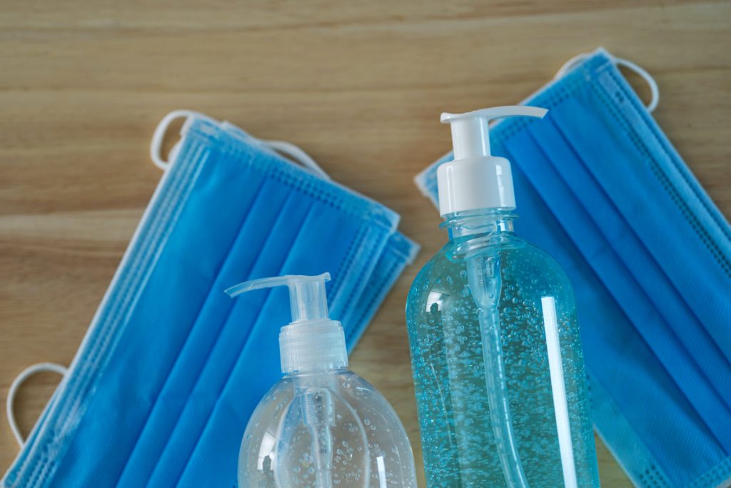 Two bottles of hand sanitizer placed beside blue disposable face masks on a wooden surface.