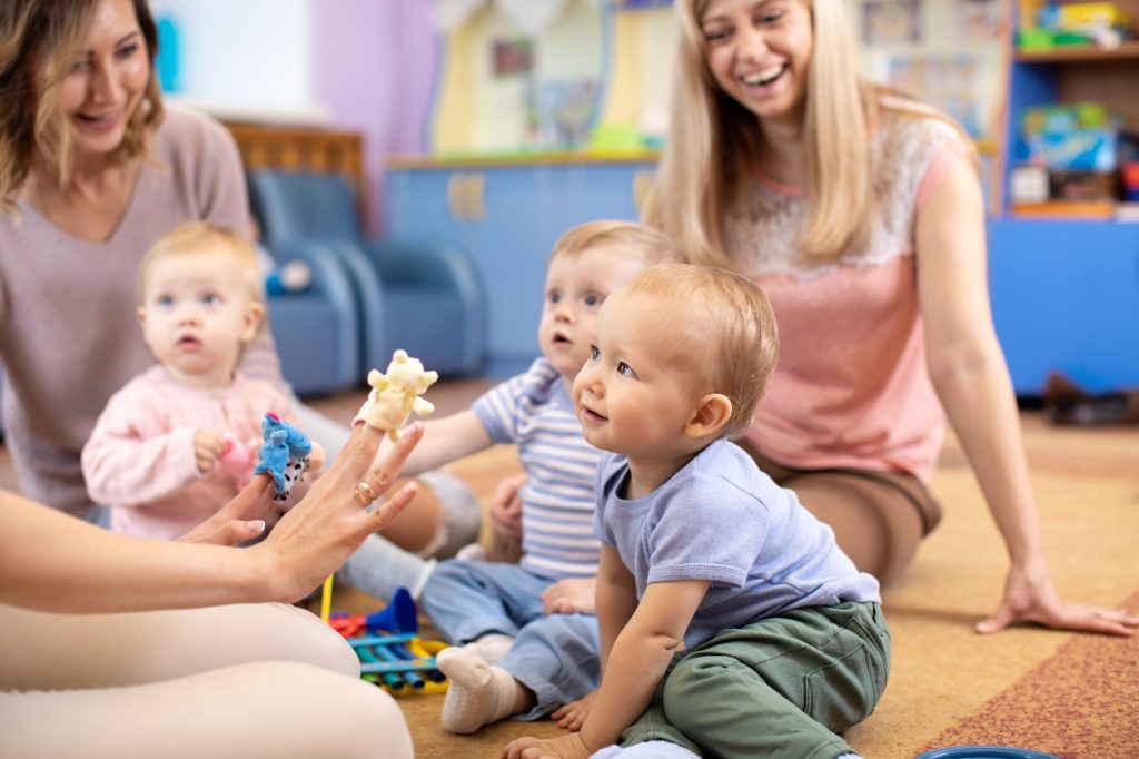 Nursery teacher and babies playing with educational toys in kindergarten or day care centre